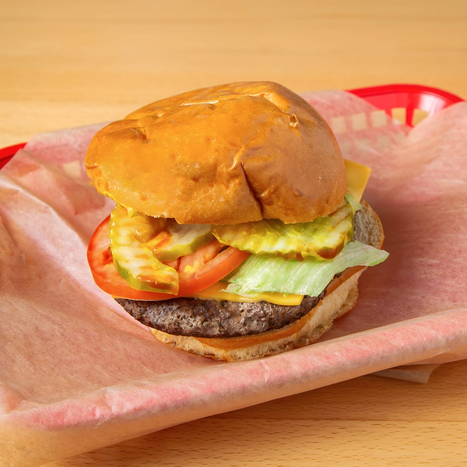 A cheeseburger with lettuce, tomato, and pickles in a red plastic basket with paper lining.