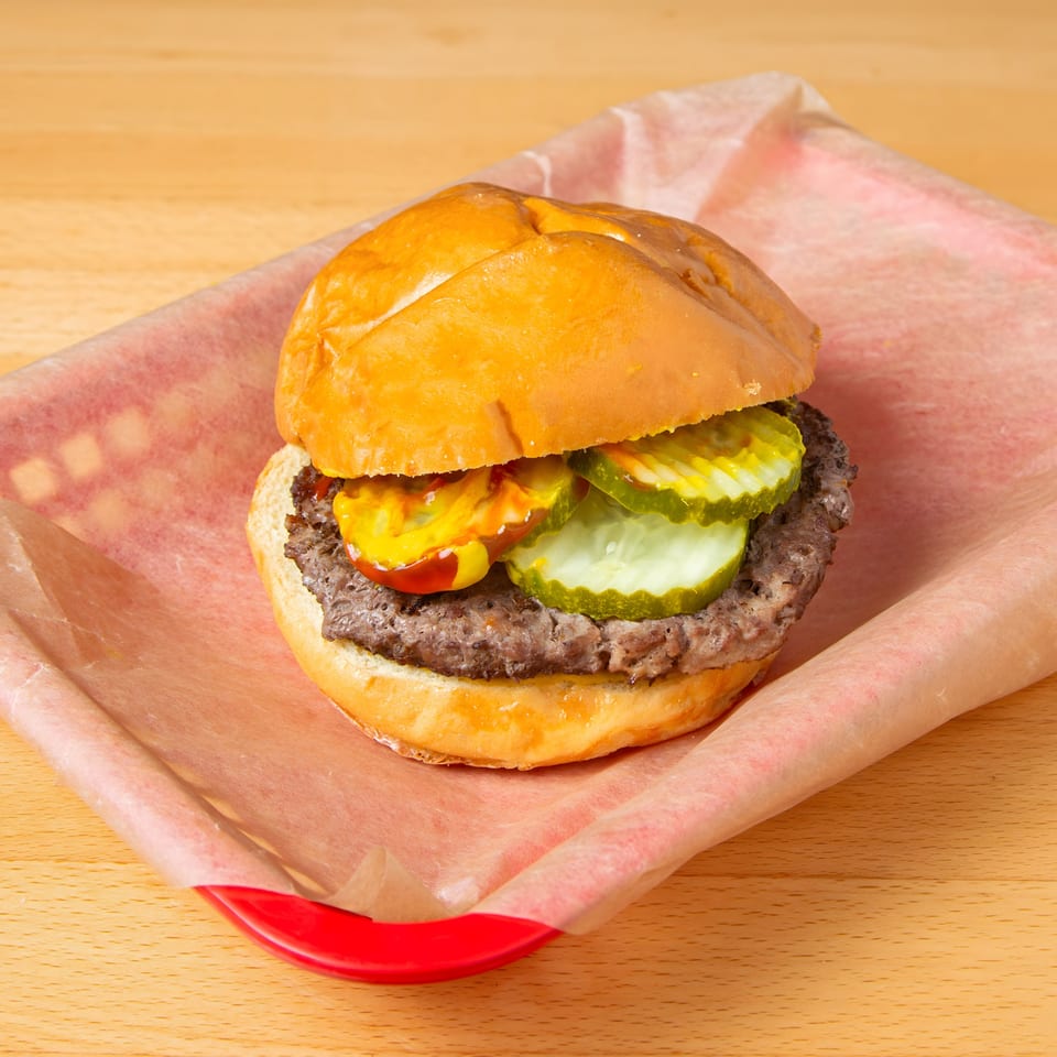 Iron Heart Pub burger with pickles, mustard, and ketchup on a red tray.