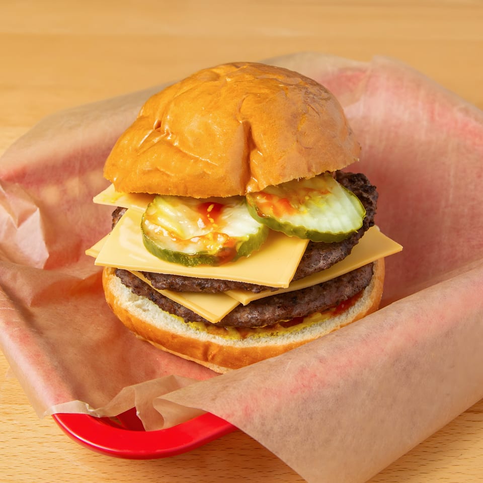 Double cheeseburger with pickles and sauce in a red basket lined with paper at Iron Heart Pub.