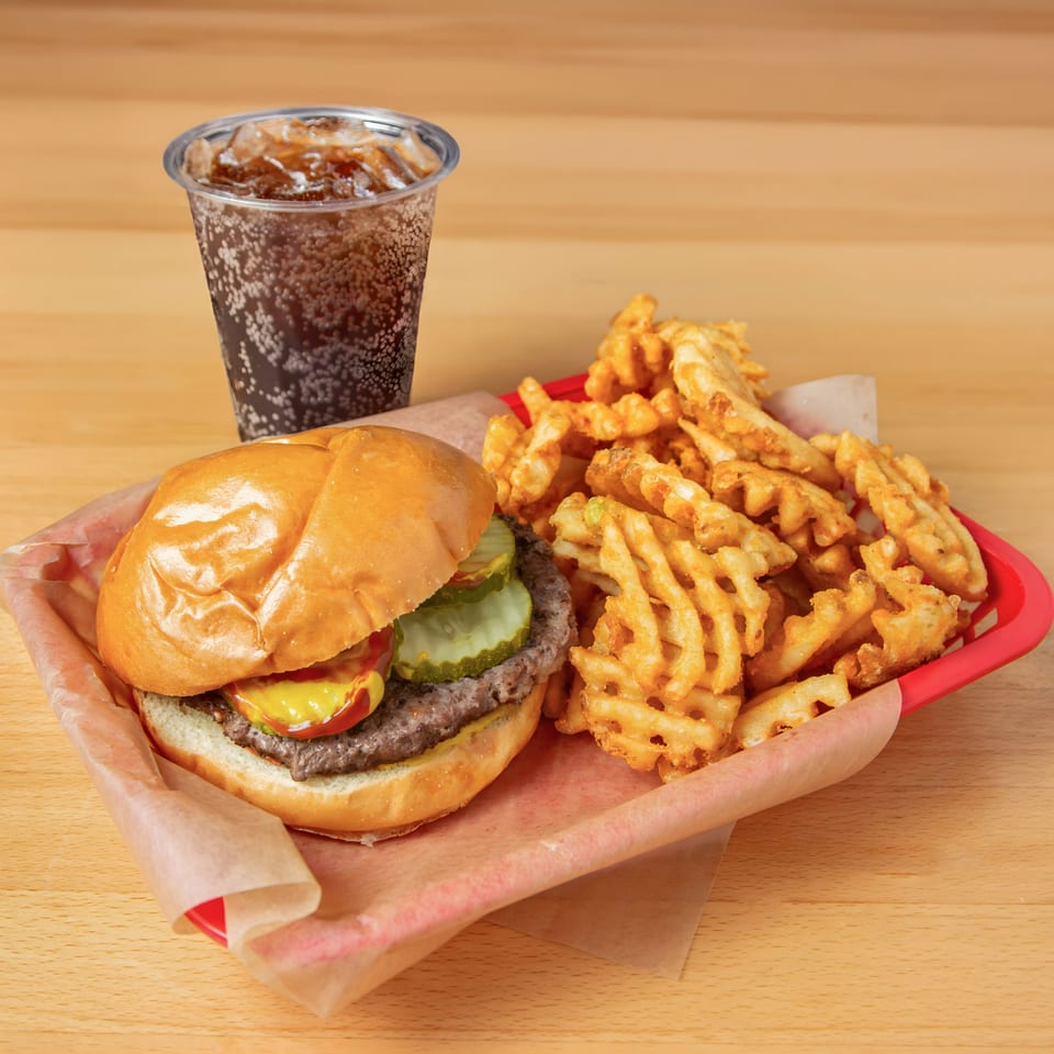 Iron Heart Pub burger with pickles, mustard, ketchup, waffle fries, and a soda.