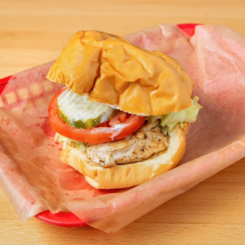 Grilled chicken sandwich with lettuce, tomato, pickles, and sauce in a red basket at Iron Heart Pub.
